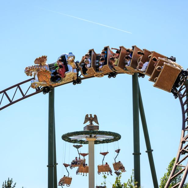 Eine Achterbahn mit Fahrgästen fährt durch einen Freizeitpark.
