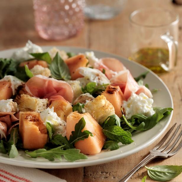 Ein Teller mit Melone, Burrata, Schinken und Rucola als Salat.