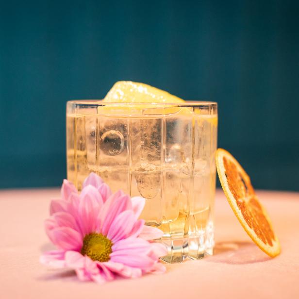 Ein Cocktail mit Eis, Zitrone und einer rosa Blume auf einem Tisch.