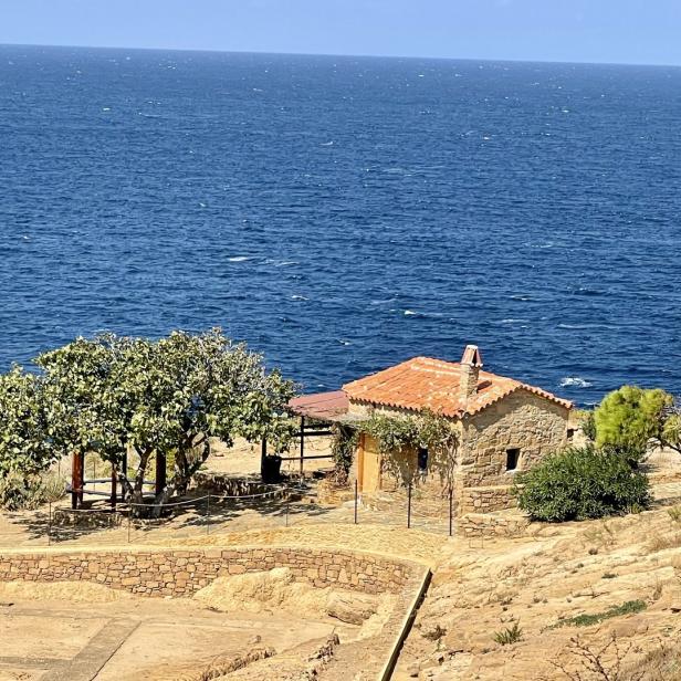 Ein kleines Steinhaus mit rotem Ziegeldach steht an der Küste mit Blick auf das Meer.
