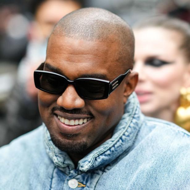 Kanye West lächelt mit Sonnenbrille und Jeansjacke.