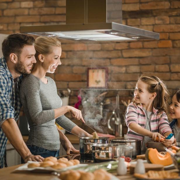 Eine Familie kocht gemeinsam in einer Küche mit Backsteinmauer.
