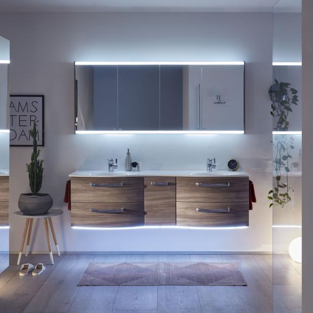 Ein modernes Badezimmer mit Holzwaschtisch, beleuchtetem Spiegel und Dekorationen.