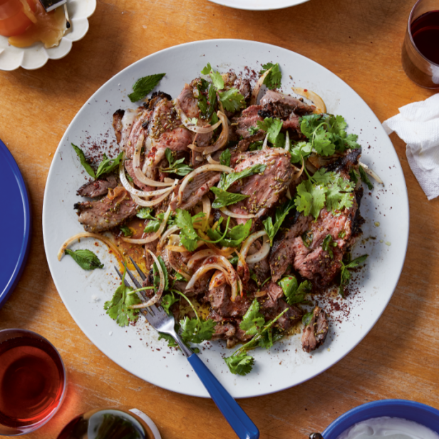 Ein Teller mit gegrilltem Fleisch, Zwiebeln und Kräutern, serviert mit Bohnen und Joghurt.