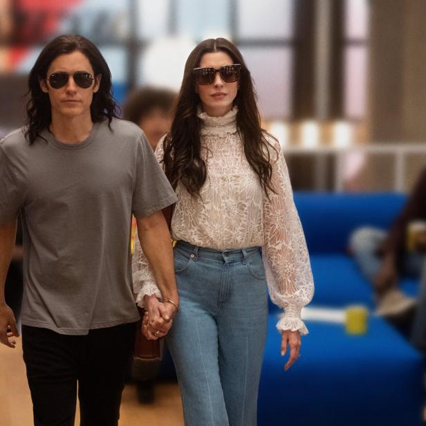 Jared Leto und Anne Hathaway gehen Händchen haltend durch einen modernen Büroraum.