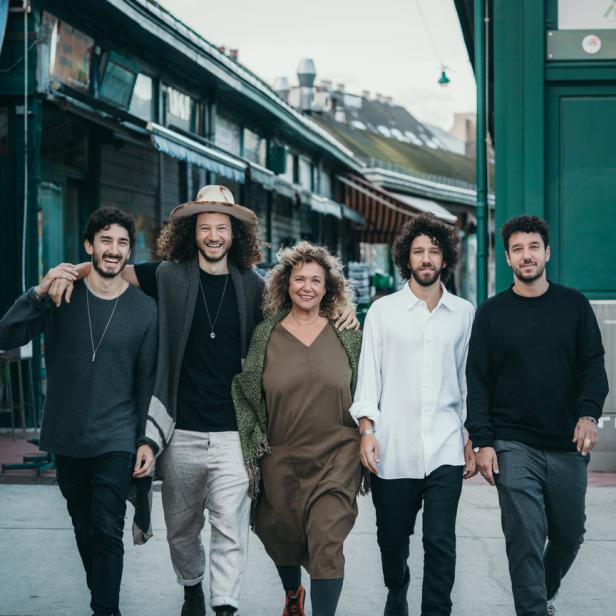 Fünf Personen gehen auf einem Gehweg vor einem Gebäude entlang.