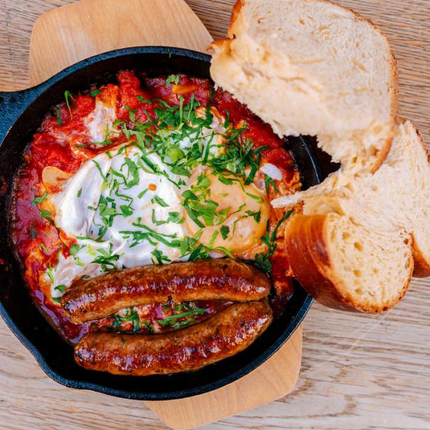 Shakshuka mit Würstchen und Brot in einer gusseisernen Pfanne.