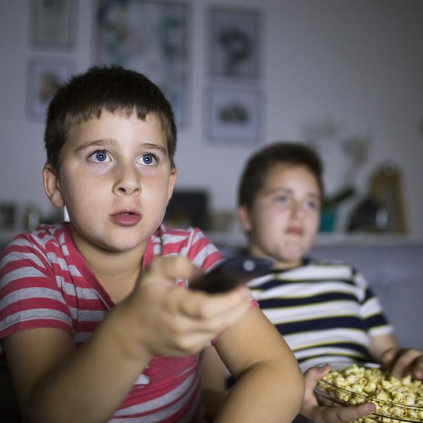 Zwei Jungen sitzen mit Popcorn auf einem Sofa und schauen fern.