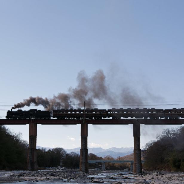 Eine Dampflokomotive fährt über eine hohe Brücke.