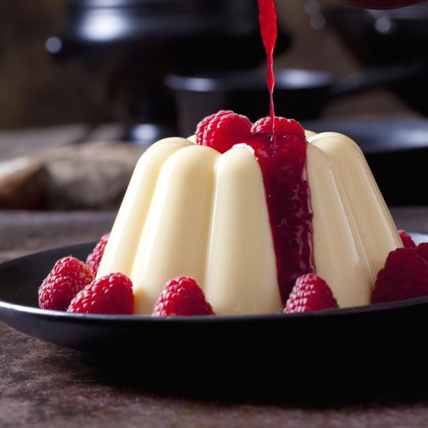 Ein Pudding wird mit Himbeersoße übergossen und mit frischen Himbeeren garniert.