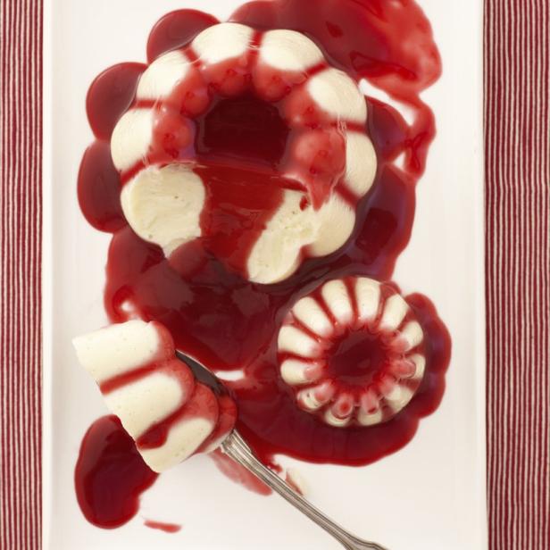 Zwei Puddingformen mit roter Sauce auf einem Teller, ein Stück davon auf einem Löffel.