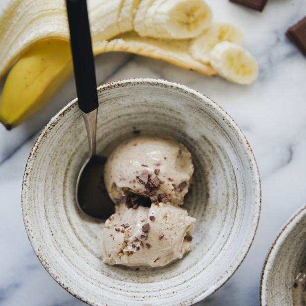Eine Schüssel mit Bananeneis, garniert mit Schokoladenstückchen, neben einer Banane und Schokoladenstücken.