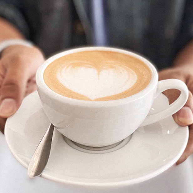 Eine Person hält eine Tasse Cappuccino mit Herzmuster im Milchschaum.