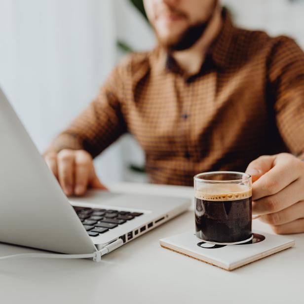 Ein Mann arbeitet am Laptop und trinkt einen Espresso.