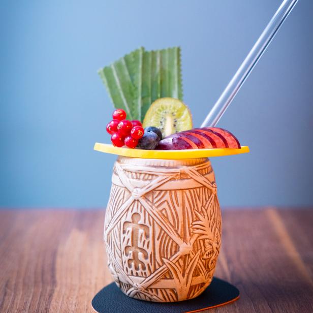 Ein Tiki-Cocktail mit Kiwi, Johannisbeeren und einer Scheibe Orange garniert.