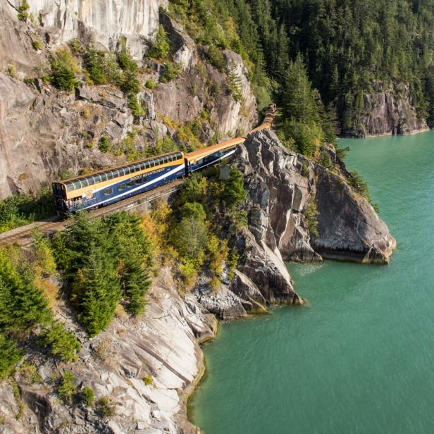 Der Rocky Mountaineer Zug fährt entlang einer Klippe am Ufer eines Sees.