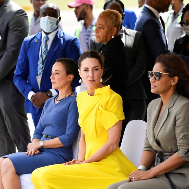 Kate Middleton sitzt in einem gelben Kleid neben zwei Frauen.