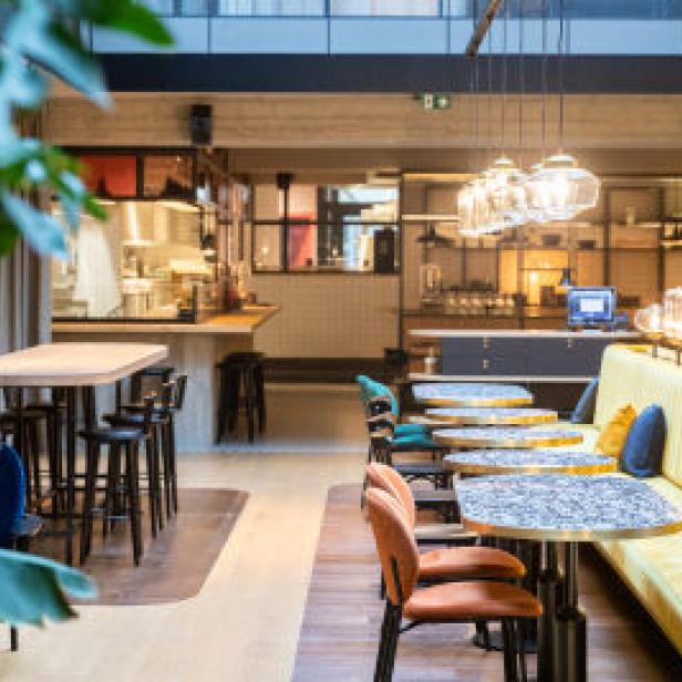 Ein Innenraum mit Tischen, Stühlen und einer gelben Sitzbank in einem Restaurant oder Café.