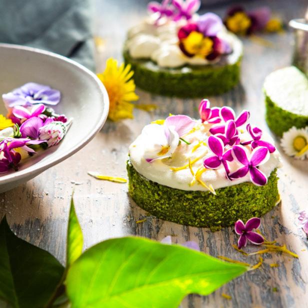 Kleine grüne Kuchen mit weißer Glasur und essbaren Blüten verziert.