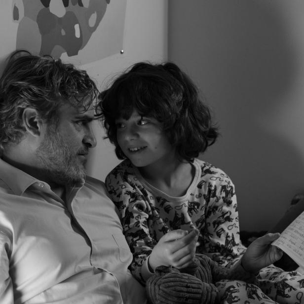 Joaquin Phoenix liest einem Kind im Bett eine Geschichte vor.