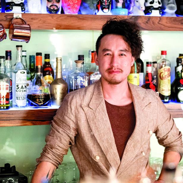 Ein Barkeeper steht vor einem Regal mit Spirituosenflaschen.
