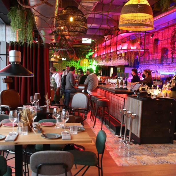 Innenansicht eines Restaurants mit Tischen, Stühlen und einer Bar.