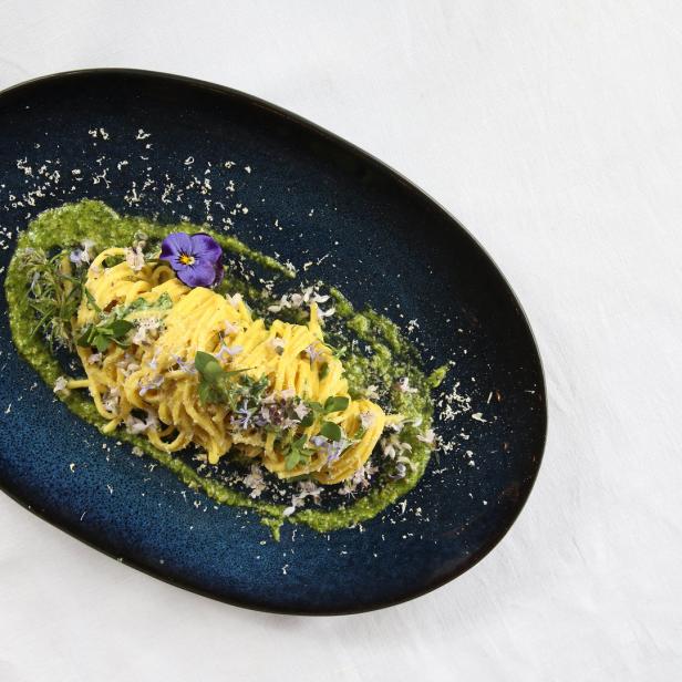 Ein Teller Spaghetti mit Pesto, essbaren Blüten und geriebenem Käse.