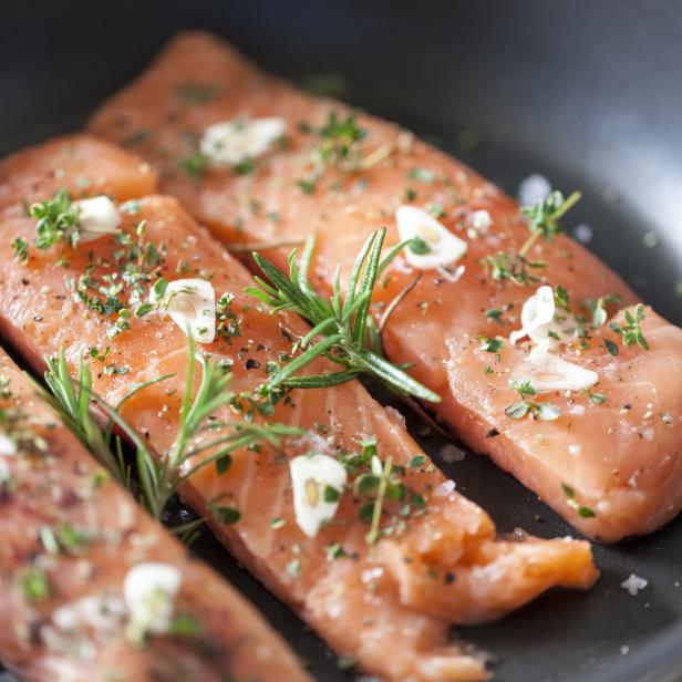 Rohe Lachsfilets mit Knoblauch, Rosmarin und Thymian in einer Pfanne.