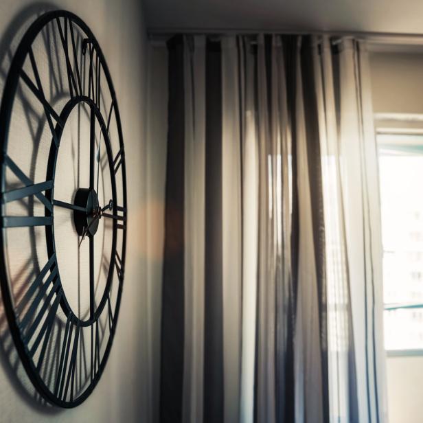 Eine große, dekorative Wanduhr hängt neben einem Fenster mit Vorhängen.