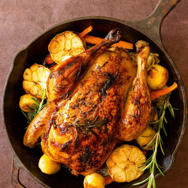 Ein gebratenes Huhn mit Knoblauch, Kartoffeln, Karotten und Rosmarin in einer gusseisernen Pfanne.