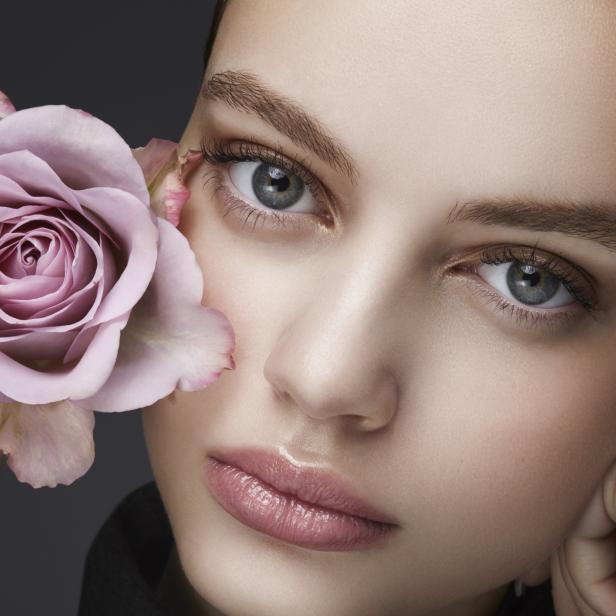 Das Porträt einer Frau mit einer rosa Rose vor ihrem Gesicht.