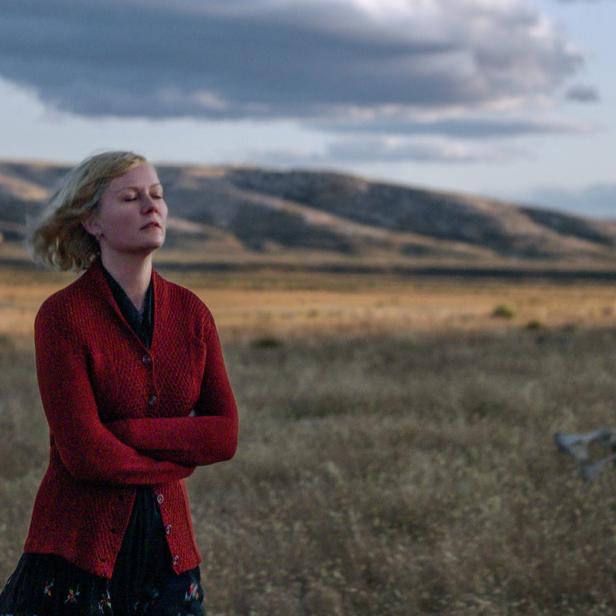 Kirsten Dunst steht mit geschlossenen Augen in einem Feld vor einem Haus.