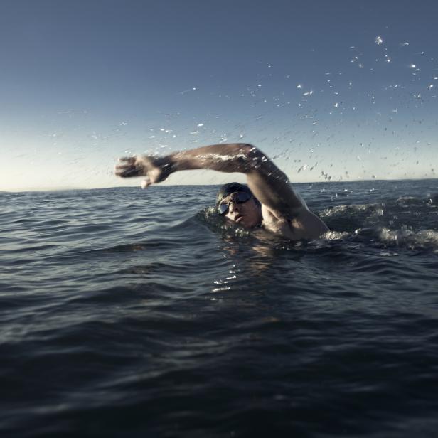 Ein Schwimmer mit Schwimmbrille krault im offenen Meer.