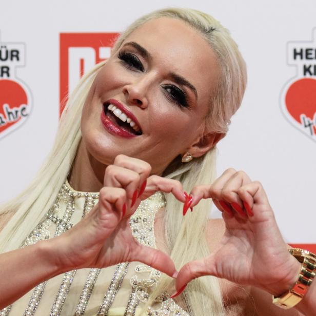 Jenny Frankhauser formt mit ihren Händen ein Herz vor einem „Ein Herz für Kinder“-Logo.