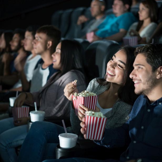 Ein junges Paar schaut im Kino einen Film und isst Popcorn.