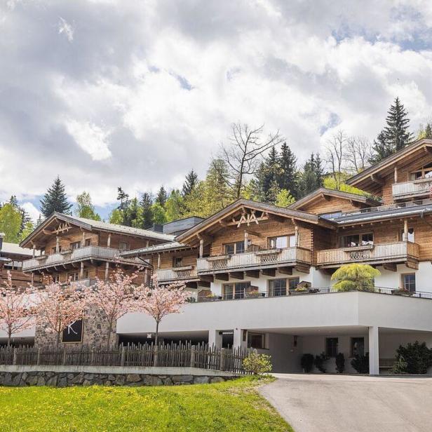 Mehrere Chalets mit Holzbalkonen vor einem bewaldeten Hügel.