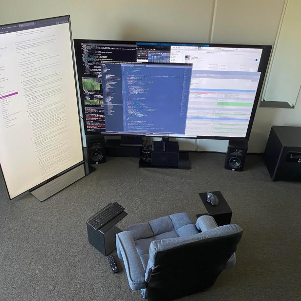 Ein Sessel steht vor zwei großen Monitoren, auf denen Code und Dokumentation angezeigt werden.
