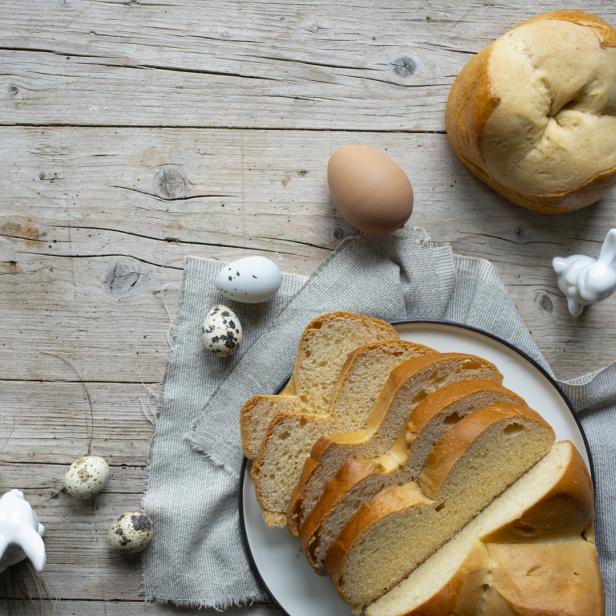 Ein Osterbrot, Eier und kleine Hasenfiguren auf einem Holztisch.