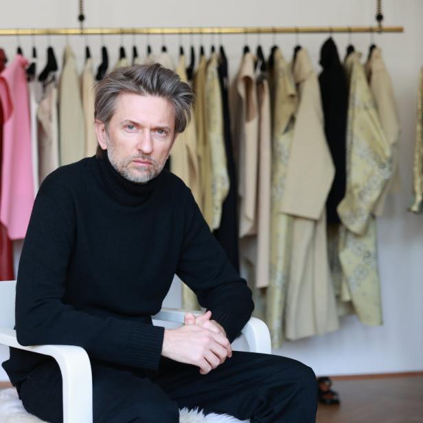 Petar Petrov sitzt in seinem Wiener Atelier vor einer Kleiderstange.