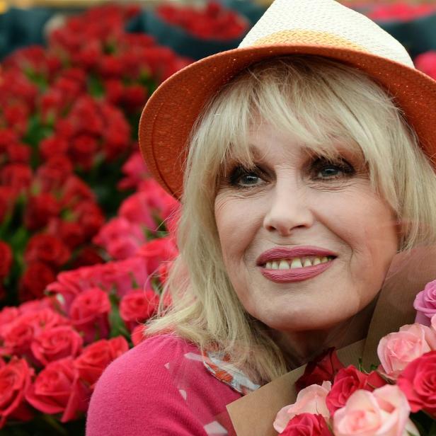 Joanna Lumley hält einen Strauß Rosen vor einem Hintergrund aus roten Rosen.