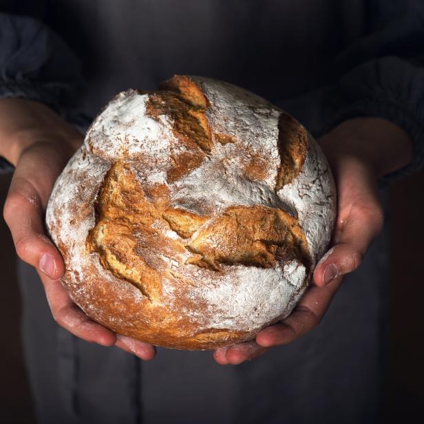 Ein Laib Sauerteigbrot wird von Händen gehalten.