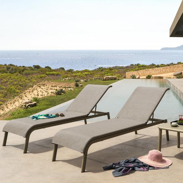 Zwei Liegestühle stehen an einem Pool mit Blick auf das Meer.