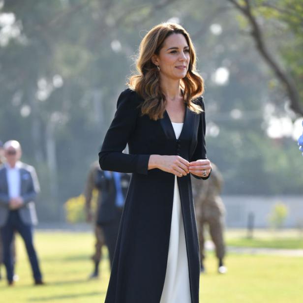 Kate Middleton trägt ein schwarzes Kleid über einem weißen Hosenanzug.