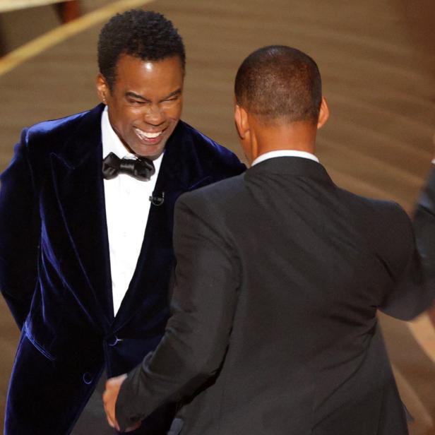 Chris Rock lacht, während Will Smith sich ihm auf der Bühne nähert.