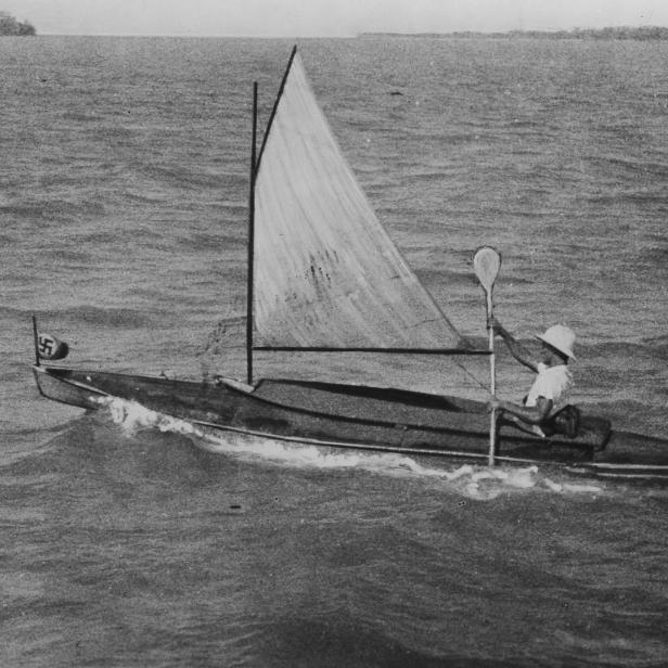 Eine Person segelt mit einem kleinen Segelboot, das eine Flagge mit einem Hakenkreuz trägt.