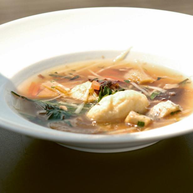 Eine Schüssel mit klarer Suppe, Gemüse und einer Nockerl.