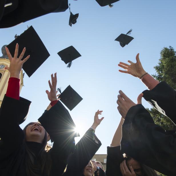 Absolventen werfen ihre Hüte in den blauen Himmel.