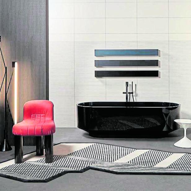 Ein Badezimmer mit einer schwarzen Badewanne, einem roten Stuhl und einem geometrischen Teppich.