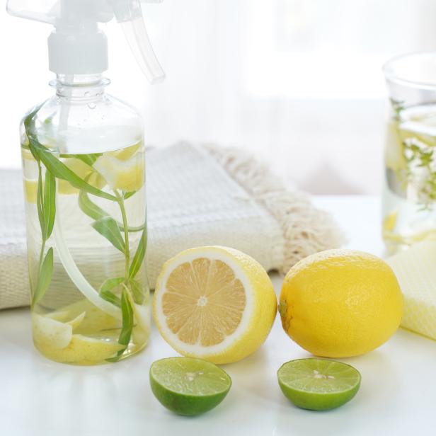 Eine Sprühflasche mit Zitronen und Kräutern steht neben Zitronen und Limetten.