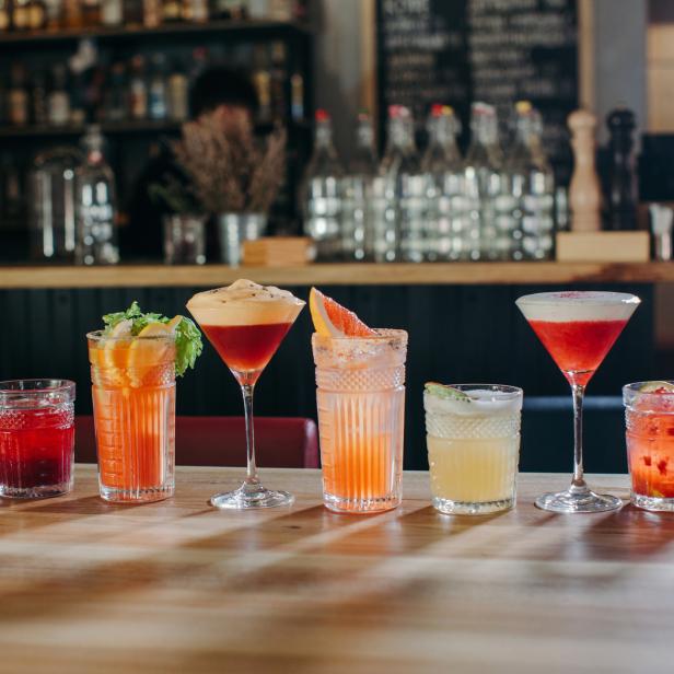 Eine Reihe von bunten Cocktails stehen auf einem Holztisch in einer Bar.